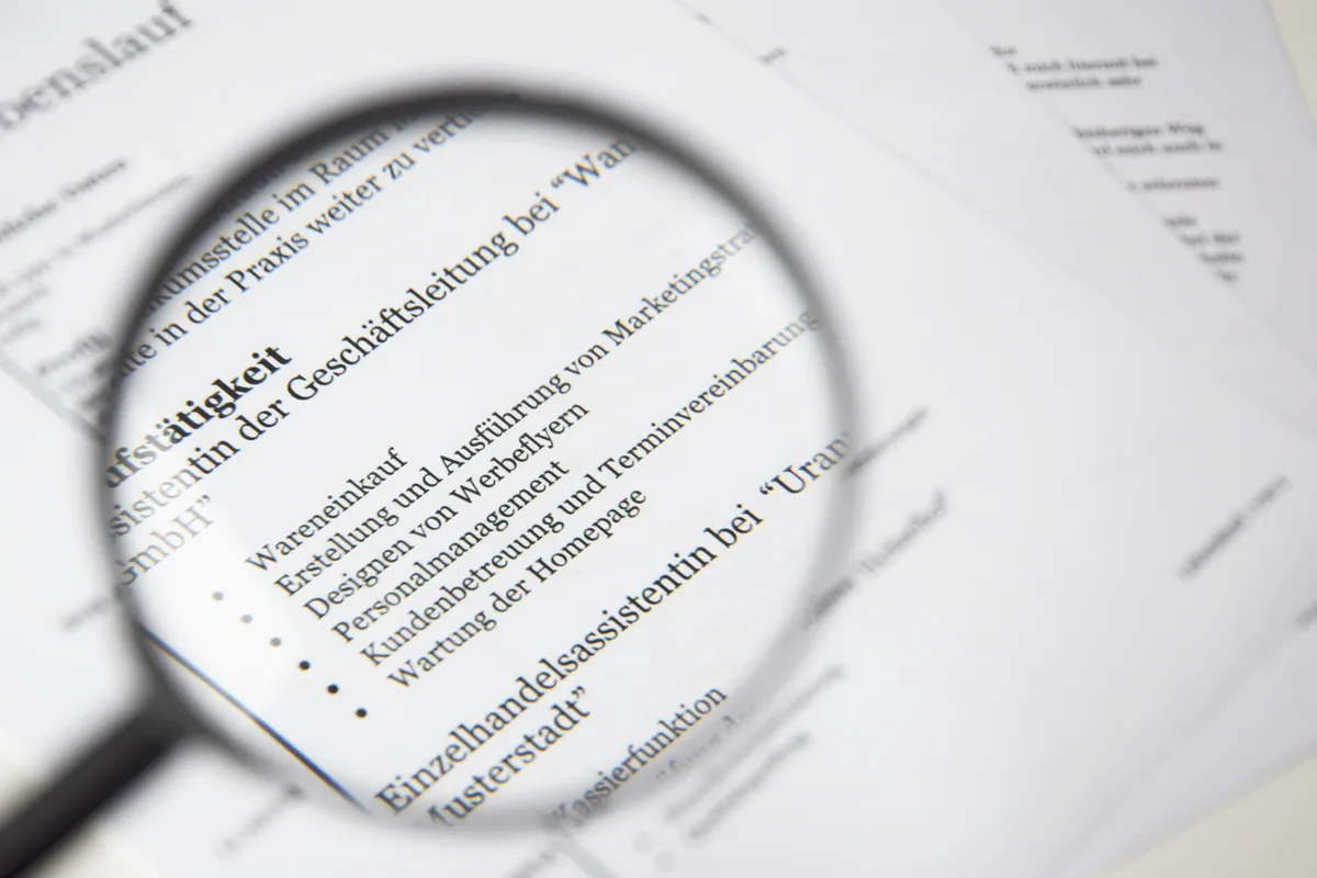 A printed resume on a desk being reviewed with a magnifying glass